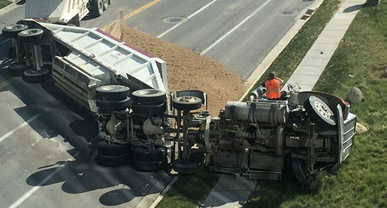 fotografia tirada de cima mostrando um caminhão após tombamento de carga em rodovia com carga esparramada na estrada